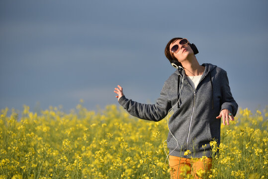 Woman with headphones listening to music in a yellow canola flower field