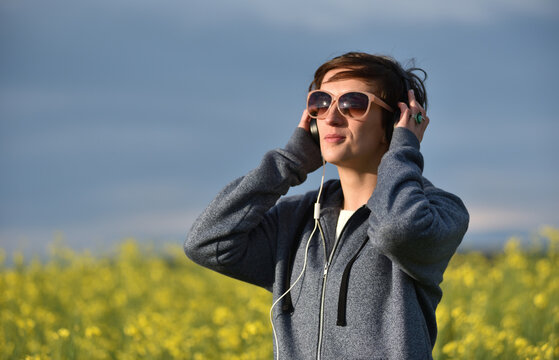 Woman with headphones listening to music in a yellow canola flower field