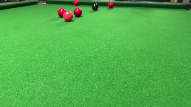 A partial triangle arrangement of snooker balls rests on a green baize table cloth, featuring six standard red balls with a single pink ball placed precisely at the apex point.