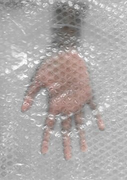 A human hand pressed flat against a sheet of transparent bubble wrap, creating a textured and distorted view of the fingers and palm.