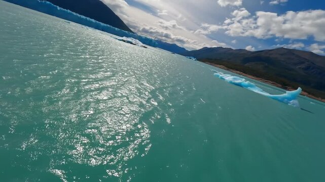 FPV drone flies just above a vivid blue iceberg floating on Lago Argentino near Perito Moreno Glacier, El Calafate, Santa Cruz, Argentina, revealing turquoise glacial water and floating ice, FPV fly