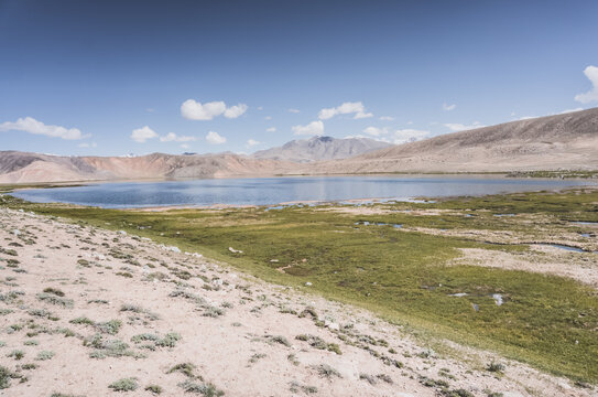 Clear-water rivers and lakes in a mountain valley, pastures and green grassy fields set against mountain ranges and snow-capped, glacier-clad peaks&mdash;a scenic landscape background