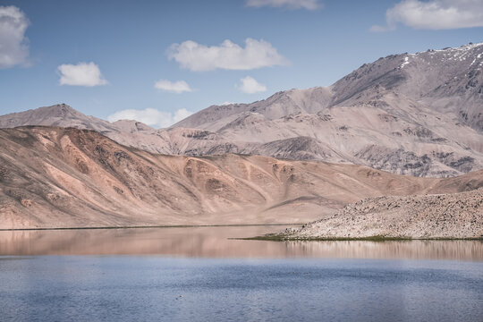 Clear-water rivers and lakes in a mountain valley, pastures and green grassy fields set against mountain ranges and snow-capped, glacier-clad peaks&mdash;a scenic landscape background