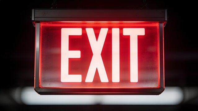 Close-up of illuminated red exit sign with bold white lettering in dark environment