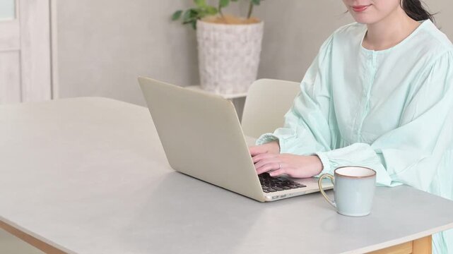 リビングでノートパソコンを使って作業する30代女性の手元