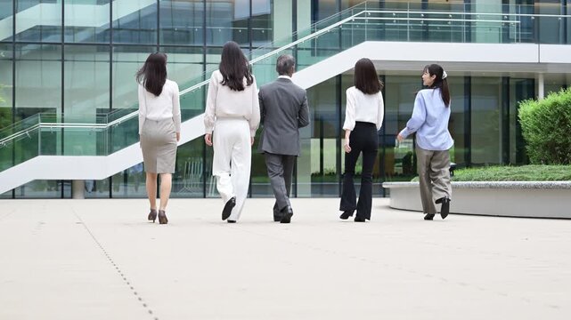 並んで歩く20代から50代の日本人ビジネスパーソン5人の後ろ姿