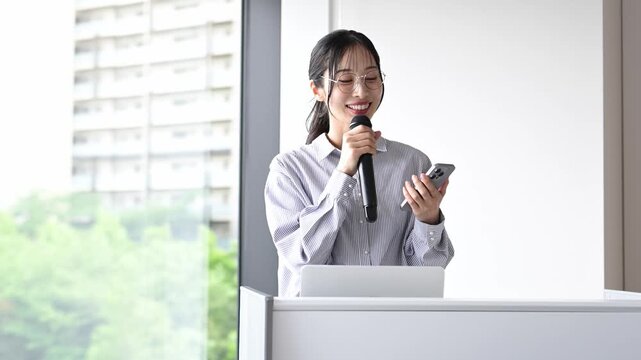 会議室でスマートフォンを持ってプレゼンテーションを行う30代の日本人ビジネスパーソンの女性