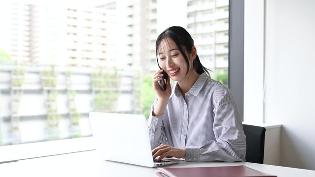 笑顔で通話をしながらノートパソコンを使う30代日本人女性