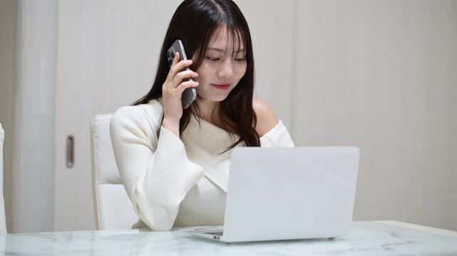 ノートパソコンを見ながら笑顔で通話をする20代日本人女性