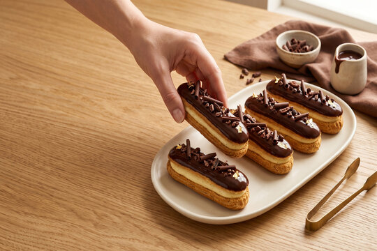 Chocolate eclair platter with vanilla custard filling, chocolate glaze, and hand reaching for pastry