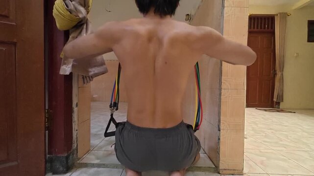 Rear view landscape of man doing bent arm rear delt fly with resistance band at home