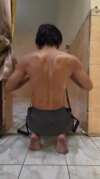Back View of Athletic Man Performing Bent Arm Rear Delt Fly Exercise Using Resistance Band at Home