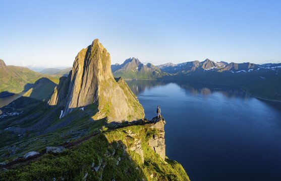 Young man in front of impressive landscape, iconic mountain Segla with steeply sloping cliffs, mountain landscape at Medfjorden fjord, evening light at sunset, Senja island, Troms, Norway