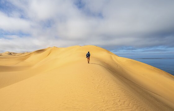 Lonely person, man with camera running on a dune, sand dunes and sea, Atlantic coast and sandy desert with sea of dunes, Sandwich Harbour, Namib Naukluft Park, Namib Desert, Namibia