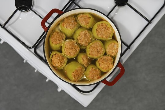 Bell peppers stuffed with minced lamb meat are cooked in cast iron pot on stove, top view