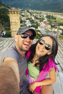 Caucasian tourist couple sit on Svan tower rooftop taking selfie watch sunset town panorama of Mestia, Svaneti, Georgia
