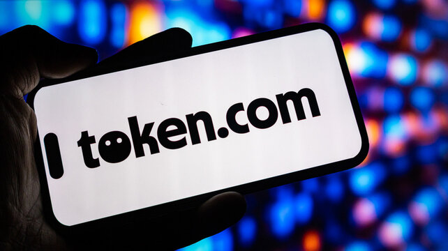 Token.com logo on smartphone screen held in hand with digital blurry background out of focus and bokeh lights.
