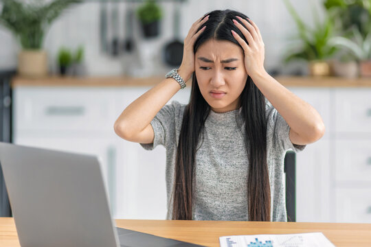 Stressed Asian woman holding head at laptop