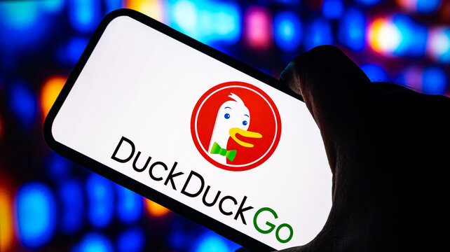 DuckDuckGo company logo on mobile phone screen held by hand with blurred multi colored neon bokeh lighting.
