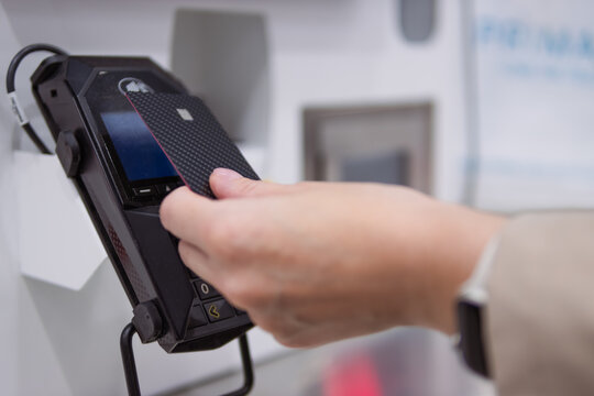 Customer making a quick and secure wireless transaction by tapping a credit card with nfc chip on a point of sale terminal, enabling modern finance and retail convenience