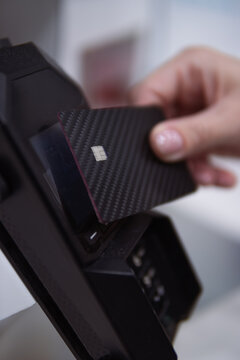 Hand swiping a carbon fiber credit card into a point of sale terminal, completing a secure chip transaction for modern digital payment and banking