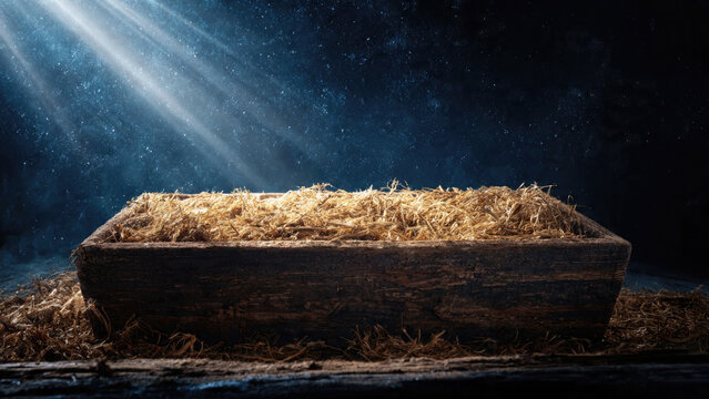 Empty wooden manger filled with straw under a dramatic night sky with light rays
