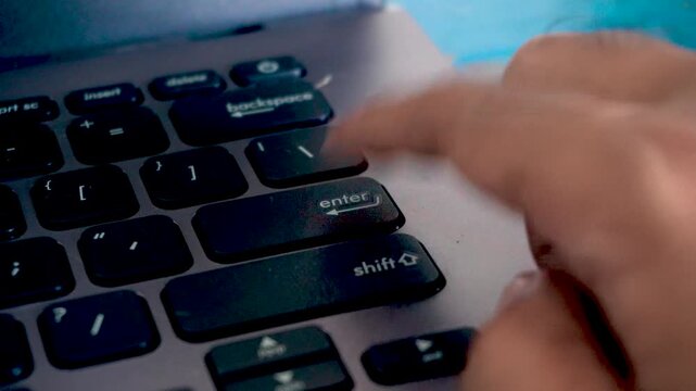 Close up of a person pressing the enter key repeatedly on a computer laptop keyboard, highlighting digital office work, data entry tasks, and technology use.