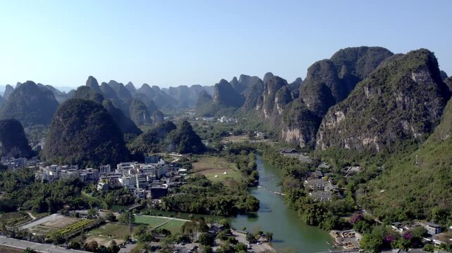 Aerial view of karst mountains, a winding river, and settlements in a lush rural valley under clear sky.