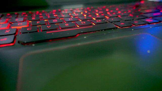 Smooth sideways slide movement capturing a macro close up view of a laptop computer keyboard with glowing red backlit keys, highlighting gaming technology and office work.