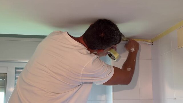 Professional male painter applying masking tape to a wall for renovation
