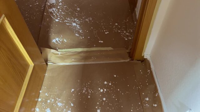 Splashed white paint on protective paper covering a wooden floor
