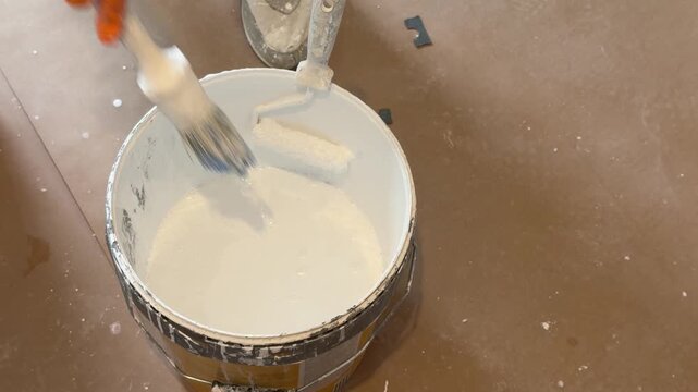 Professional painter dipping a brush into a bucket of white paint