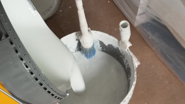 Painter pouring white paint into a bucket for house renovation