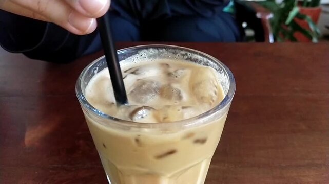 Stir a glass of cold latte coffee using a straw until mixed. Slow motion mode