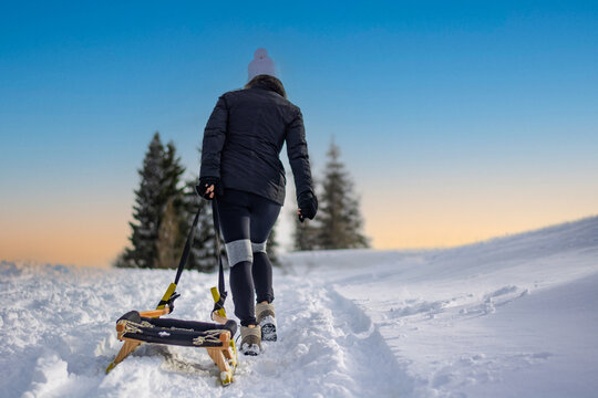 A determined woman walks uphill through deep snow pulling an elegant wooden sled on a beautiful winter day