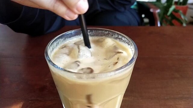 Stir a glass of cold latte coffee using a straw until mixed