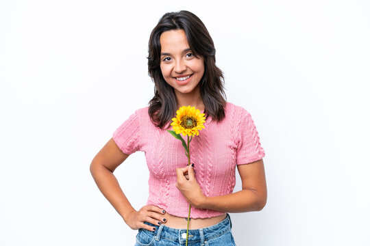Young hispanic woman holding sunflower isolated on white background posing with arms at hip and smiling