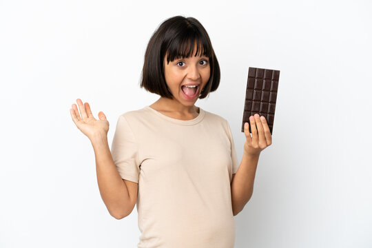 Young mixed race pregnant woman isolated on white background taking a chocolate tablet and surprised