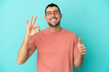 Fototapeta premium Young handsome caucasian man isolated on blue background With glasses and doing OK sign