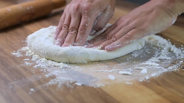 Close up baker hands kneading fresh pizza dough on wooden board with flour, traditional Italian cooking in pizzeria kitchen