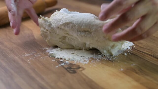 Close up baker hands kneading fresh pizza dough on wooden board with flour, traditional Italian cooking in pizzeria kitchen