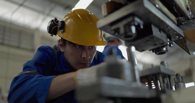 Focused factory worker in blue coverall operating and adjusting metal press machine in factory