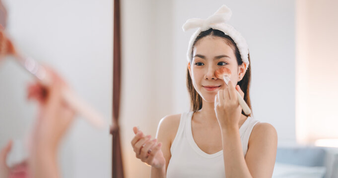 Young adult southeast asian woman makeup and face skincare before mirror in dress room at home