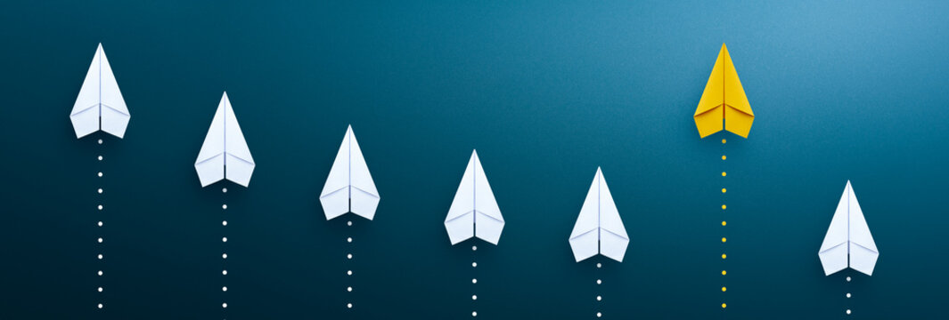 Business growth and stand out from the crowd concept with flying yellow paper planes on blue background