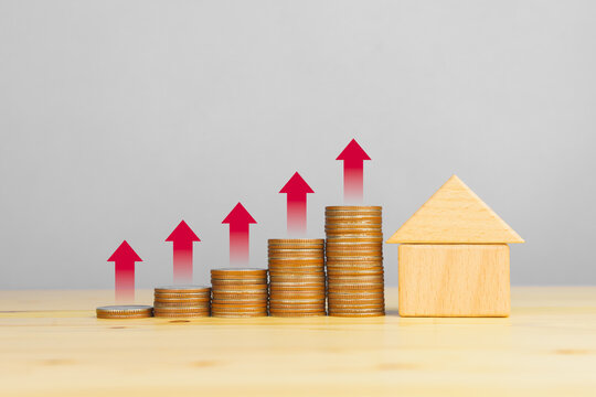 Rising property value concept, stacked coins with red upward arrows and wooden house model