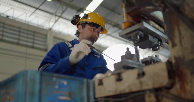 Focused factory worker in blue coverall operating and adjusting metal press machine in factory