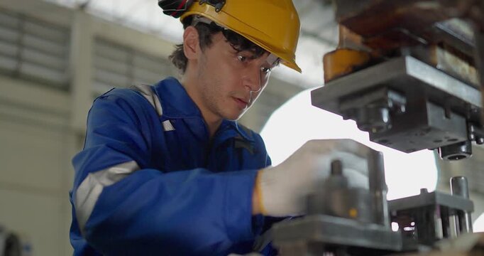 Focused factory worker in blue coverall operating and adjusting metal press machine in factory