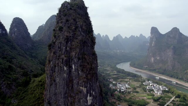 A scenic landscape of tall karst peaks, a winding river, and rural settlements under overcast skies.