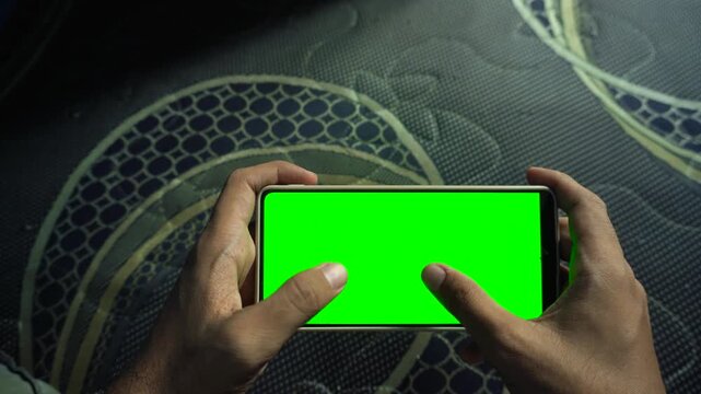 Static horizontal smartphone display with a green screen held by a person playing a mobile game, capturing clean device mockups, chroma key technology, and digital media concepts.