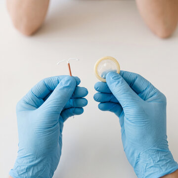 Close-up of hands in medical gloves holding an intrauterine device and condom for contraception choice